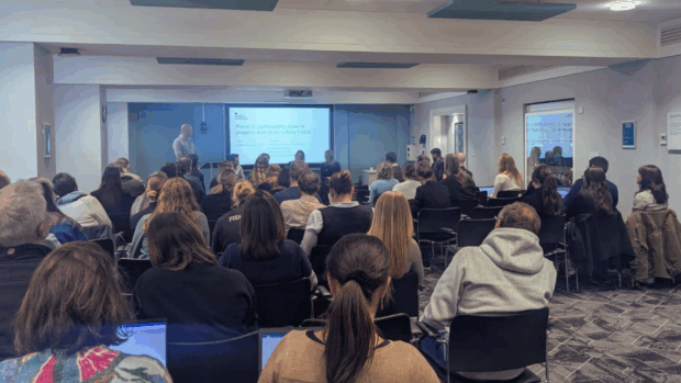 A crowd of individuals sitting in chairs, focused on a presentation in a conference room