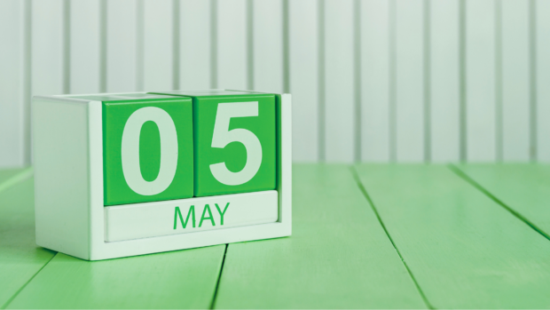 A calendar displaying May 5th rests on a wooden table, highlighting the date against a natural wood background.